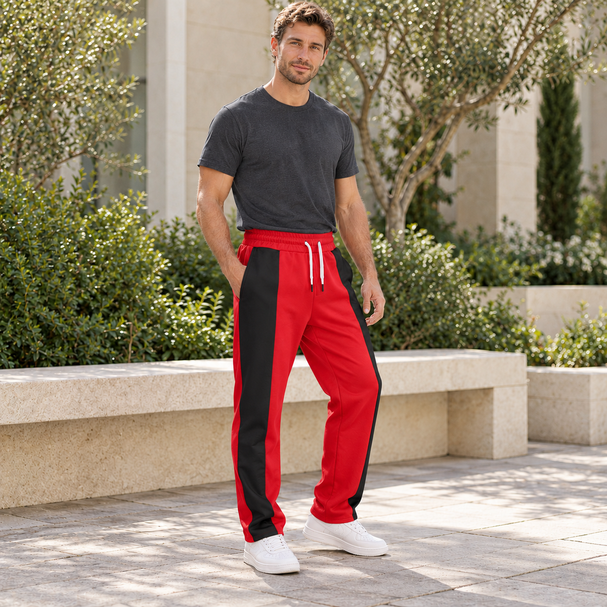 Adult male model wearing red and black colorblock straight-leg pants in a sunlit courtyard
